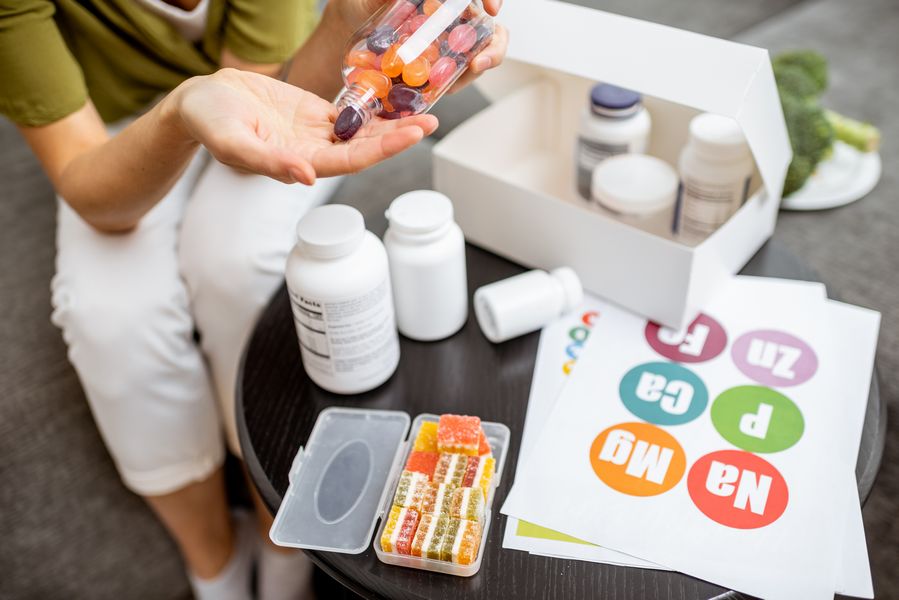 kobieta biorąca suplementy w otoczeniu opakowań po suplementach i kasetki na tabletki Blog Zdrowe Dębniki
